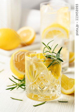 Summer refreshing lemonade drink or alcoholic cocktail with ice, rosemary and lemon slices on the white table. Summer refreshing lemonade drink or alcoholic cocktail with ice, rosemary and lemon slices on the white table. 113458993