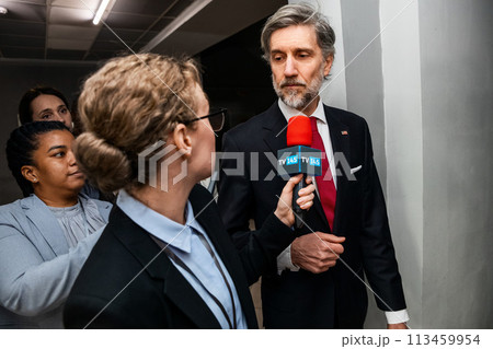 American politician walks in corridor of government building, answers press questions 113459954