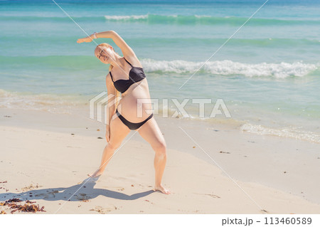 Harmonizing mind and body, a pregnant woman gracefully practices yoga on the beach, embracing the serenity of the seaside for a tranquil and mindful pregnancy experience 113460589