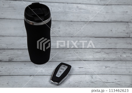 A car key with automatic buttons and a thermocup are black with metal inserts on a white wood background with a place for text. High quality photo A car key with automatic buttons and a thermocup are black with metal inserts on a white wood background with a place for text. High quality photo 113462623