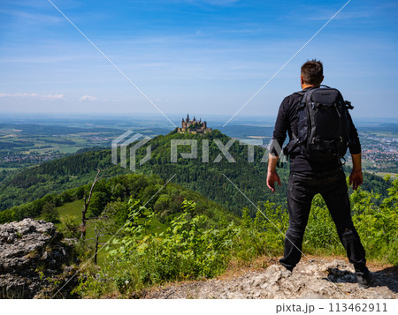 a traveler with a backpack stands on a mountain against the backdrop of a castle a traveler with a backpack stands on a mountain against the backdrop of a castle 113462911