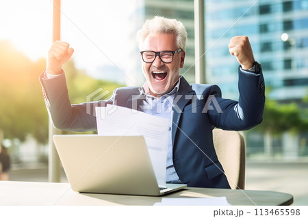 A man with glasses sitting at a desk, using a laptop computer and smiling A man with glasses sitting at a desk, using a laptop computer and smiling 113465598
