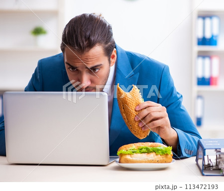 Young male employee having breakfast at workplace Young male employee having breakfast at workplace 113472193