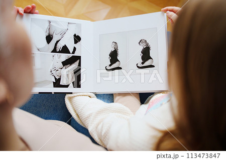 mother and daughter flips through a book with photos of dad and pregnant mom. mother and daughter flips through a book with photos of dad and pregnant mom. 113473847