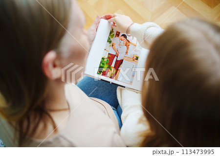 mother and daughter flips through a book with photos of dad and pregnant mom. mother and daughter flips through a book with photos of dad and pregnant mom. 113473995
