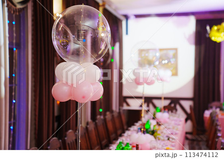 Large transparent, pink and white balloons on blurred holiday table background. 113474112