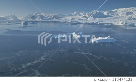 Polar Ocean on Snow Mountains Background. Antarctica Aerial Drone View Flight. Overwhelming Scene of Ice Cold Ocean Water With Icebergs. Sunlit Mountain Range. Winter Antarctic Landscape. 113474122