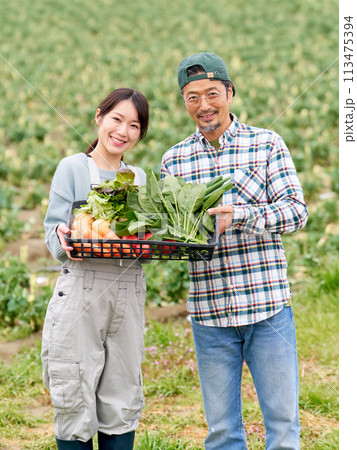 農作物をかかえて笑顔を見せる若い女性とベテラン農夫 113475394