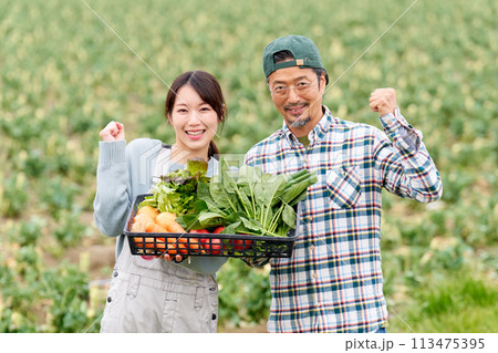 畑の前でガッツポーズをする若い女性とベテラン農夫 113475395