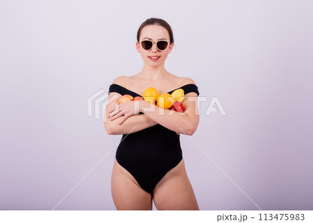A female holding apples, lemons, oranges in different arms isolated on grey background. A female holding apples, lemons, oranges in different arms isolated on grey background. 113475983