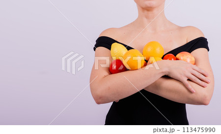 A female holding apples, lemons, oranges in different arms isolated on grey background. 113475990