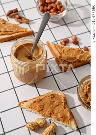 Peanut paste in a glass jar with a spoon, on a light background. Peanut paste in a glass jar with a spoon, on a light background. 113477666