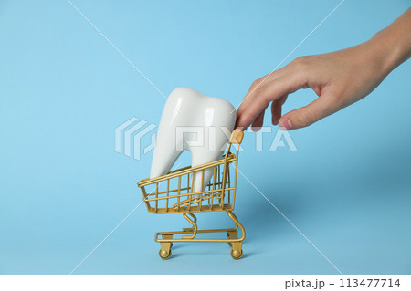 Tooth in shopping cart and hand on blue background Tooth in shopping cart and hand on blue background 113477714