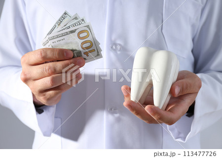 Dollars and tooth in hands of dentist on gray background 113477726