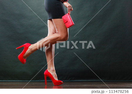 Girl in black short dress red spiked shoes holds handbag 113478256