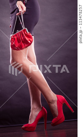 Girl in black short dress red spiked shoes holds handbag 113478257