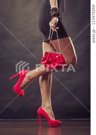 Girl in black short dress red spiked shoes holds handbag 113478260