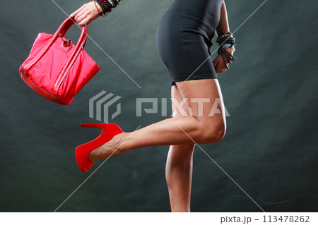Girl in black short dress red spiked shoes holds handbag 113478262