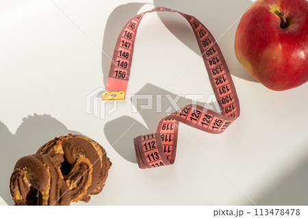 Measuring tape with cute emoji face on white background, apple and chocolate cookie shadow play Measuring tape with cute emoji face on white background, apple and chocolate cookie shadow play 113478478