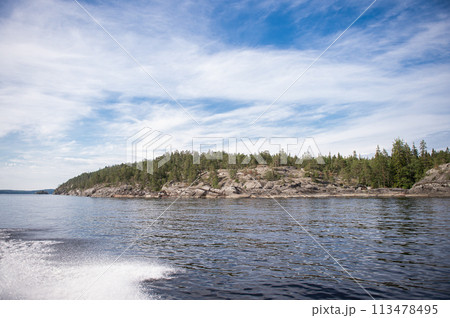 Rocky and stone river bank with fir trees on a sunny day. Water splashes from the boat, calm Rocky and stone river bank with fir trees on a sunny day. Water splashes from the boat, calm 113478495