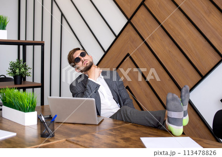 A man is sitting in the office with a laptop, his feet are on the table. Procrastinating A man is sitting in the office with a laptop, his feet are on the table. Procrastinating 113478826