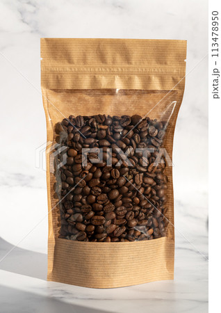 A kraft paper bag with coffee beans for viewing with a highlighted shadow lies on a white background 113478950
