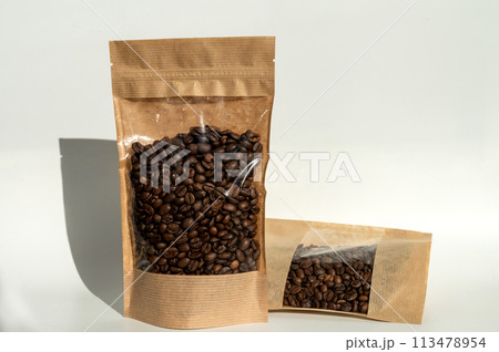 A kraft paper bag with coffee beans for viewing with a highlighted shadow lies on a white background 113478954