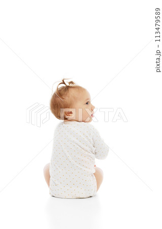 Cute little baby girl sitting in comfortable clothes and looking with curiosity isolated on white background. Careless happy kid Cute little baby girl sitting in comfortable clothes and looking with curiosity isolated on white background. Careless happy kid 113479589