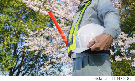 春の桜を背景に誘導棒とヘルメットを持つ作業服の男性|建設業・警備業などのイメージ 春の桜を背景に誘導棒とヘルメットを持つ作業服の男性|建設業・警備業などのイメージ 113480189