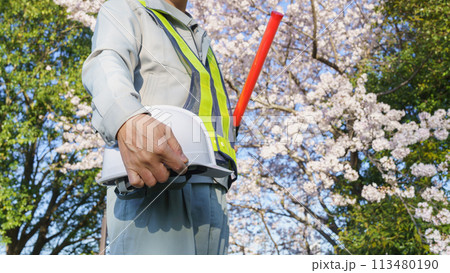 春の桜を背景に誘導棒とヘルメットを持つ作業服の男性|建設業・警備業などのイメージ 春の桜を背景に誘導棒とヘルメットを持つ作業服の男性|建設業・警備業などのイメージ 113480190