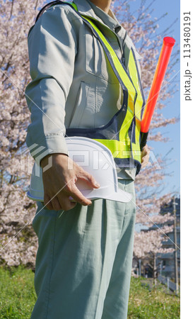 春の桜を背景に誘導棒とヘルメットを持つ作業服の男性|建設業・警備業などのイメージ 春の桜を背景に誘導棒とヘルメットを持つ作業服の男性|建設業・警備業などのイメージ 113480191