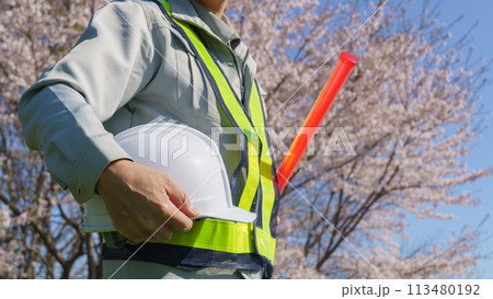春の桜を背景に誘導棒とヘルメットを持つ作業服の男性|建設業・警備業などのイメージ 春の桜を背景に誘導棒とヘルメットを持つ作業服の男性|建設業・警備業などのイメージ 113480192