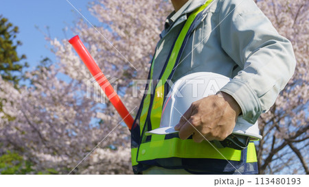 春の桜を背景に誘導棒とヘルメットを持つ作業服の男性|建設業・警備業などのイメージ 春の桜を背景に誘導棒とヘルメットを持つ作業服の男性|建設業・警備業などのイメージ 113480193