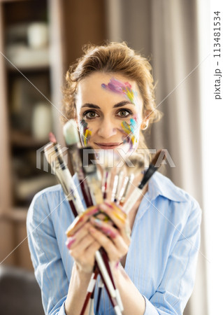 Portrait of a cute Latin woman holding a bunch of paintbrushes with both hands and smiling Portrait of a cute Latin woman holding a bunch of paintbrushes with both hands and smiling 113481534