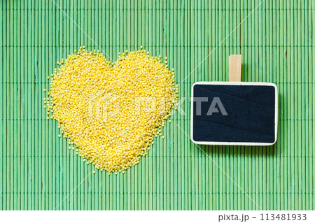 Millet groats heart shaped on green mat surface. 113481933