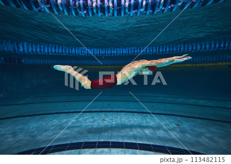 Butterfly swim style. Athletic young man, swimmer in motion training, preparing for competition, swimming in pool indoors. 113482115