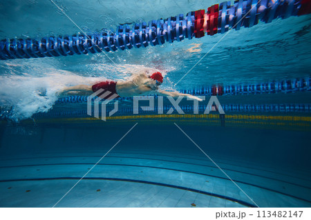Boundless energy and motivation. Athletic young man, swimmer in cap and goggles in motion training in pool indoors. 113482147
