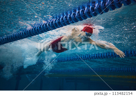 Reaching athletic achievement. Competitive, focused young man, swimmer in motion in pool indoors, training Reaching athletic achievement. Competitive, focused young man, swimmer in motion in pool indoors, training 113482154