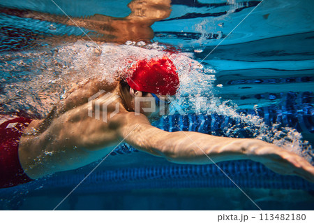 Discipline and focus. Muscular, athletic young man in red can and goggles in motion, swimming in pool, training 113482180