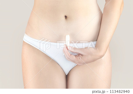Woman holding a menstruation cotton tampon in her hand, in white underwear nude beige background close up 113482940