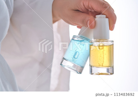 Two yellow and blue serums in a womans hands in a robe. 113483692