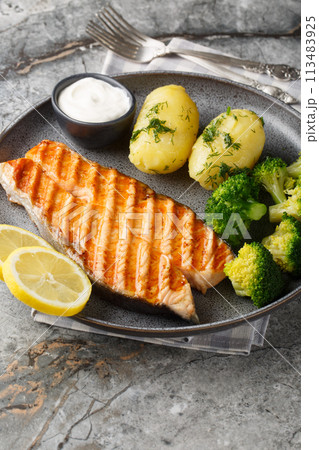 Close up of delicious grilled salmon with new potatoes, broccoli and cream sauce in a plate. Vertical 113483925