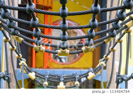 Close-up view of colorful playground rope bridge for children's outdoor recreational equipment in a public park. 113484784