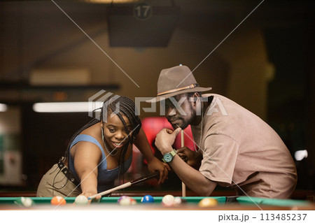 Portrait of adult African American couple playing pool together and leaning over table in nightclub 113485237