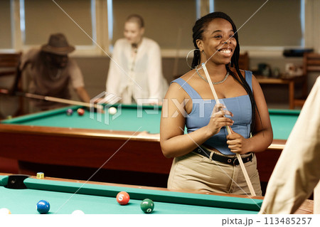 Waist up portrait of smiling African American woman chatting with friend while enjoying game of pool together in low light copy space 113485257