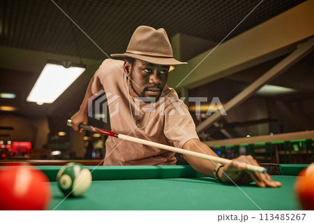 Dramatic portrait of adult African American man playing pool and hitting ball with cue stick in pool club copy space 113485267