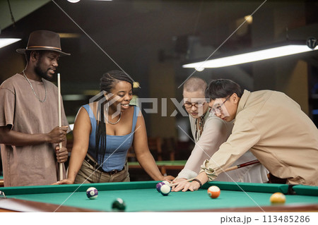 Multiethnic group of smiling young people playing pool together with Asian man taking shot at ball Multiethnic group of smiling young people playing pool together with Asian man taking shot at ball 113485286