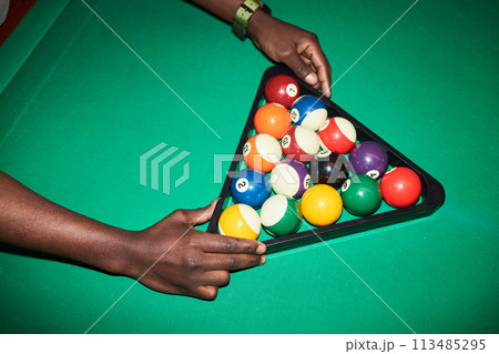 Close up of unrecognizable Black man setting billiard balls in triangle frame on green pool table shot with flash copy space 113485295