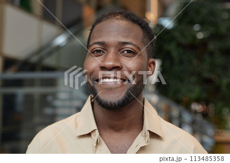 Front view portrait of young African American man smiling at camera posing in office building Front view portrait of young African American man smiling at camera posing in office building 113485358
