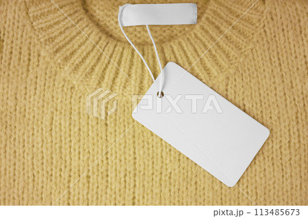 Blank clothing tag and inner label on neck of yellow knitted sweater background 113485673